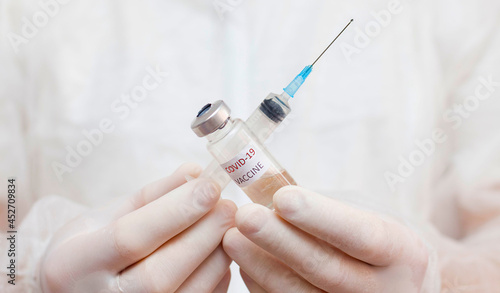 A man in a medical uniform holds an ampoule with a coronavirus vaccine in front of him.