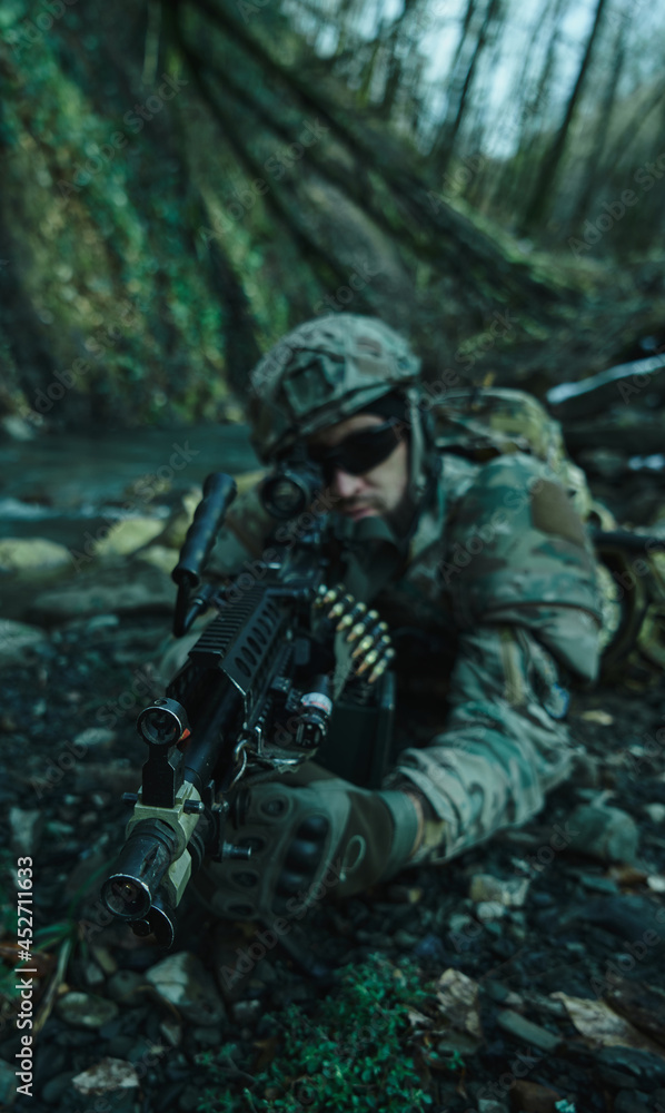 Portrait of airsoft player in professional equipment in helmet aiming at victim with gun in the forest. Soldier with weapons at war Portrait of airsoft player in professional equipment in helmet aiming at victim with gun in the forest. Soldier with weapons at war