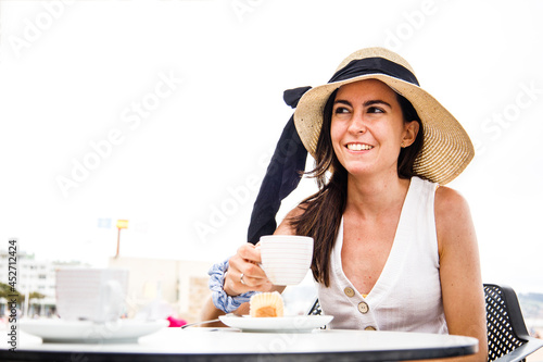 Young latinx woman with beach hat holding a cup of coffee and smiling