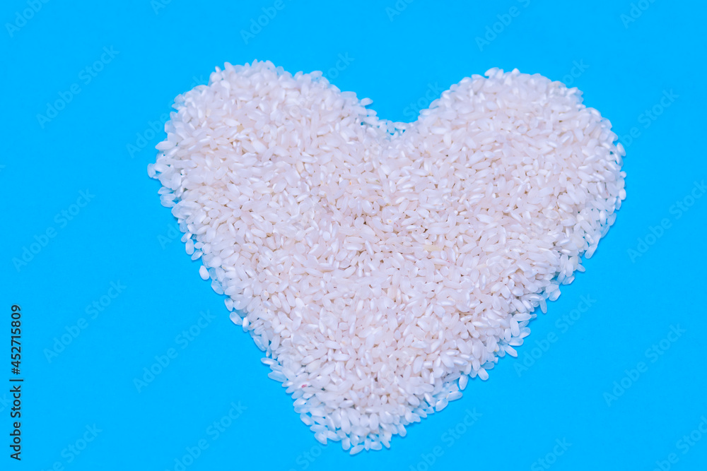 a handful of raw white rice in the shape of a heart on a blue background. concept of food, cooking and healthy life