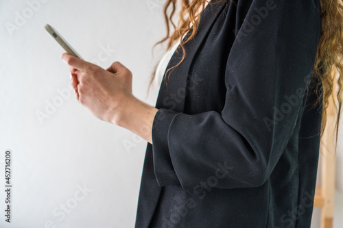 a girl with long dark hair in a black classic suit and a white top is on duty with a modern phone on a white background