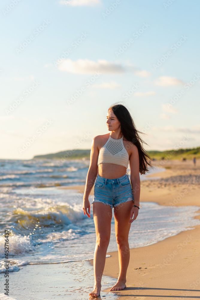 Lonely young woman walking on the beachsunset day.Beach woman in fashion beachwear relaxing walking near summer ocean. Lonely young woman walking on the beachsunset day.Beach woman in fashion beachwear relaxing walking near summer ocean.