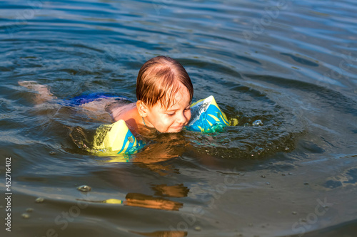 A happy child is swimming in the river on a very hot summer day. Swim in reservoirs. A happy family has fun and splashes in the water in the summer. © Alina Lebed