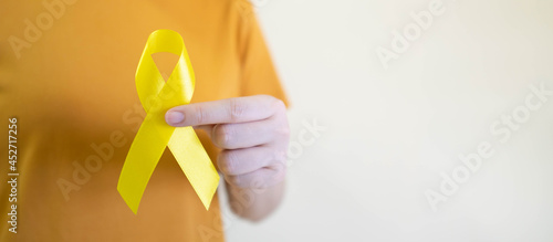 Young female holding yellow gold ribbon awareness symbol for endometriosis, suicide prevention, sarcoma bone cancer, bladder cancer, liver cancer and childhood cancer concept. Health care. Copy space.