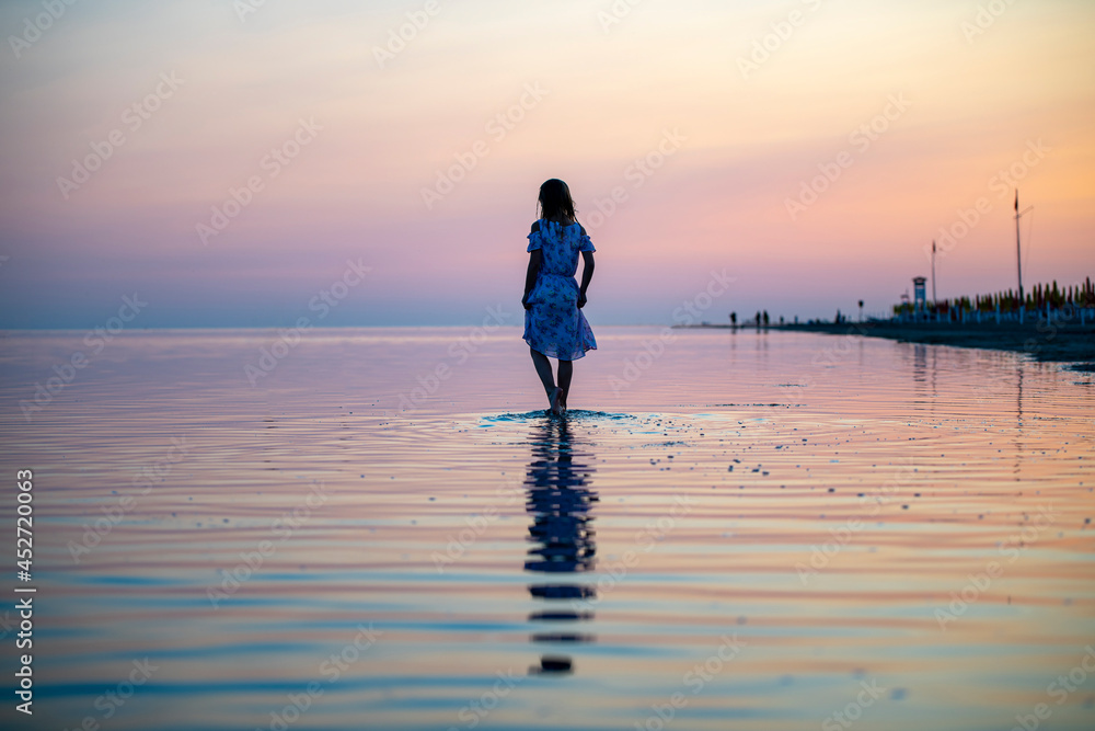 the sky and the sea merge together during a pink sunset and calm, a girl in a pink dress walks on the water