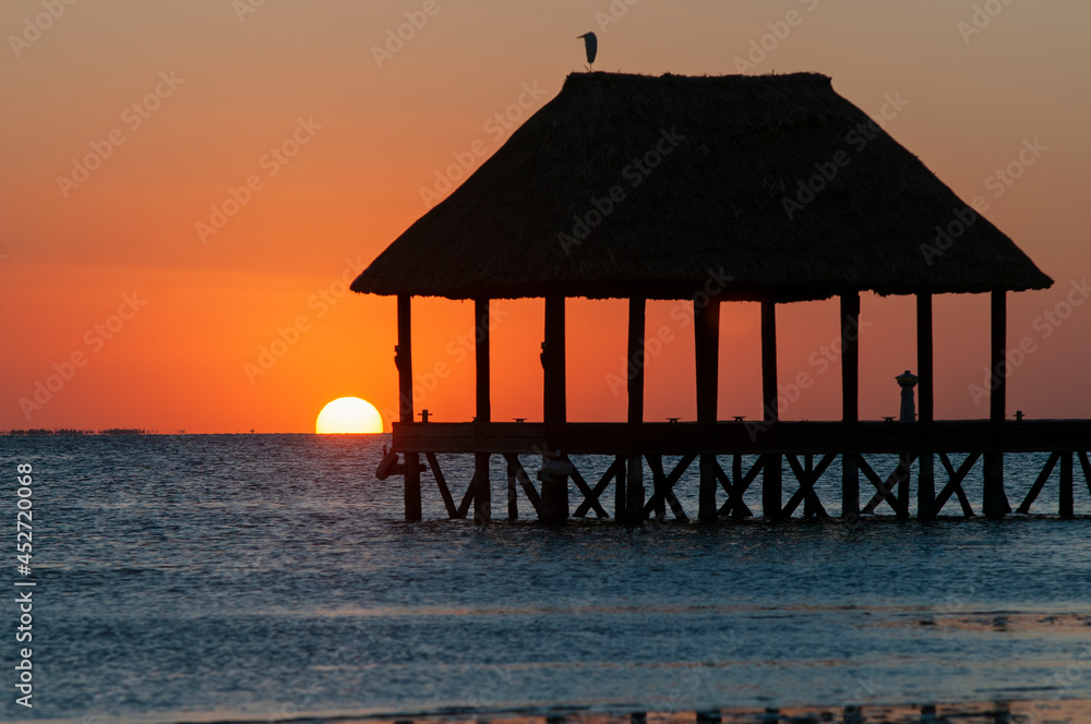 Wooden pier by the sea with thatched roof at sunset on a tropical beach on Holbox Island in Mexico