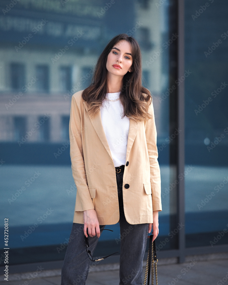 A woman stands on the background of a glass building in a jacket