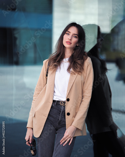 A woman stands on the background of a glass building in a jacket