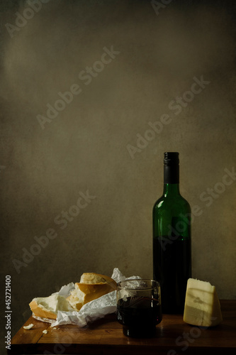 Bread, red wine and cheese on a wooden table and rustic background. Still life lighting and composition.