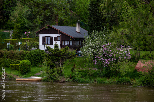 cottage on the river bank and a boat in front of it © Vladimira