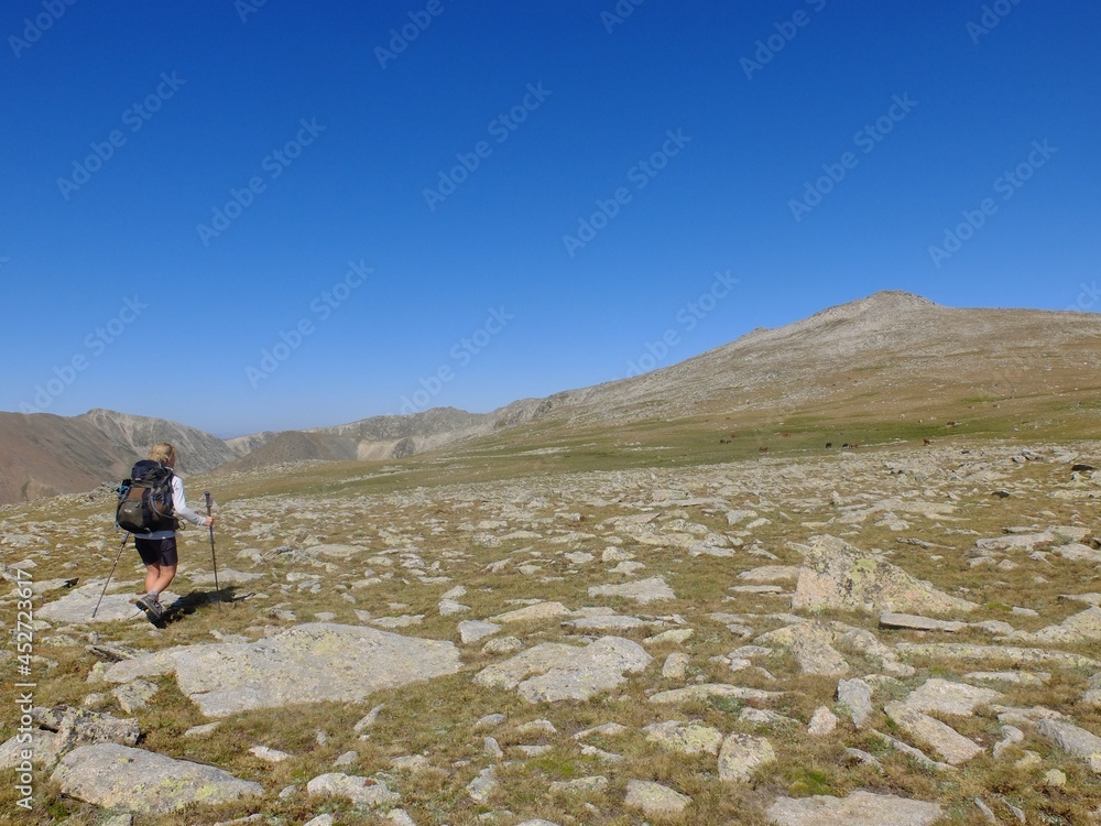 jeune femme qui randonne en montagne avec sac à dos dans les Pyrénées hors sentier dans l'herbe et les crêtes
