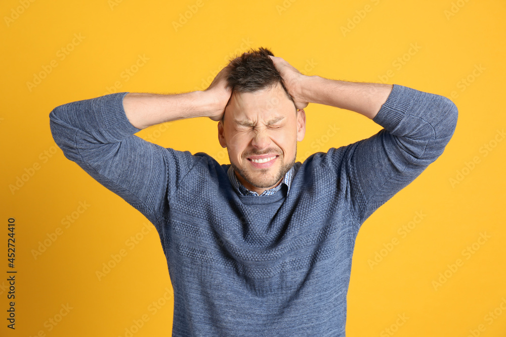 Man suffering from terrible migraine on yellow background Man suffering from terrible migraine on yellow background