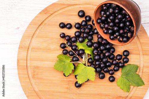 On a wooden kitchen board  black currant berries in a clay bowl and in bulk. 