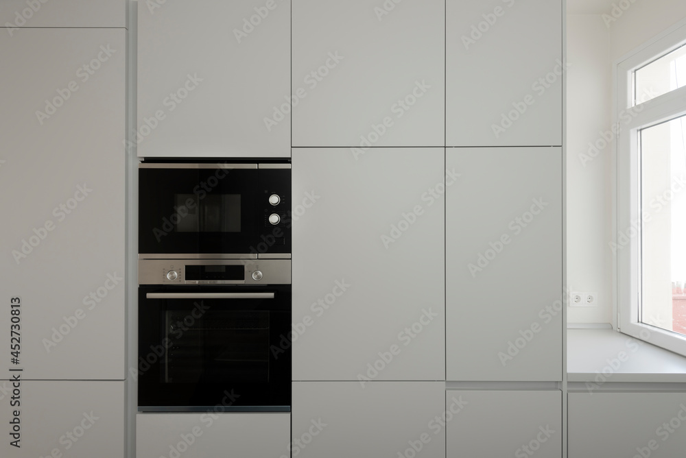 Fototapeta premium front wall of gray kitchen furniture with microwave oven and window