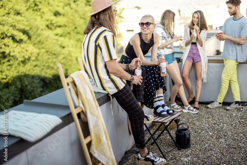 Stylish carefree persons talk and drink beer at roof top terrace at countryside house. Friends hanging out at picnic outdoors