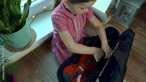 A little girl in a red dress takes out a violin from a case. View from above.