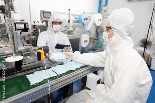 male engineers wearing personal protective equipment uniform(PPE), producing medical face mask beside machine in laboratory