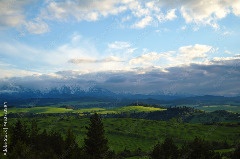 Fototapeta premium Piękne, zielone łąki podświetlone promieniami słonecznymi z widokiem na Tatry.