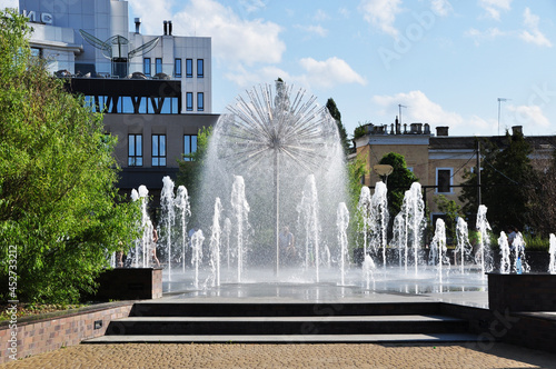 Fountain in the city square. View of a beautiful fountain and city buildings. Summer day.