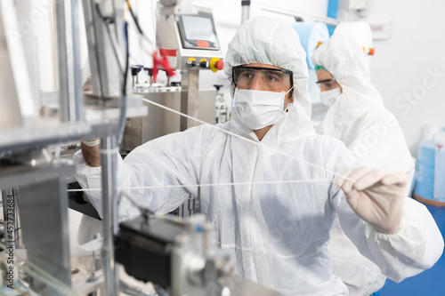 male engineers wearing personal protective equipment uniform(PPE) and medical face mask, checking machine in laboratory