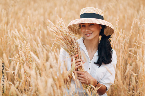 Young Woman in straw hat holding sheaf of wheat ears at agricultural field.