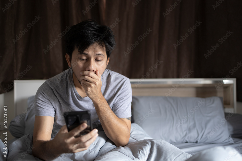 Young Asian men use a smartphone on the bed in the morning after wake up