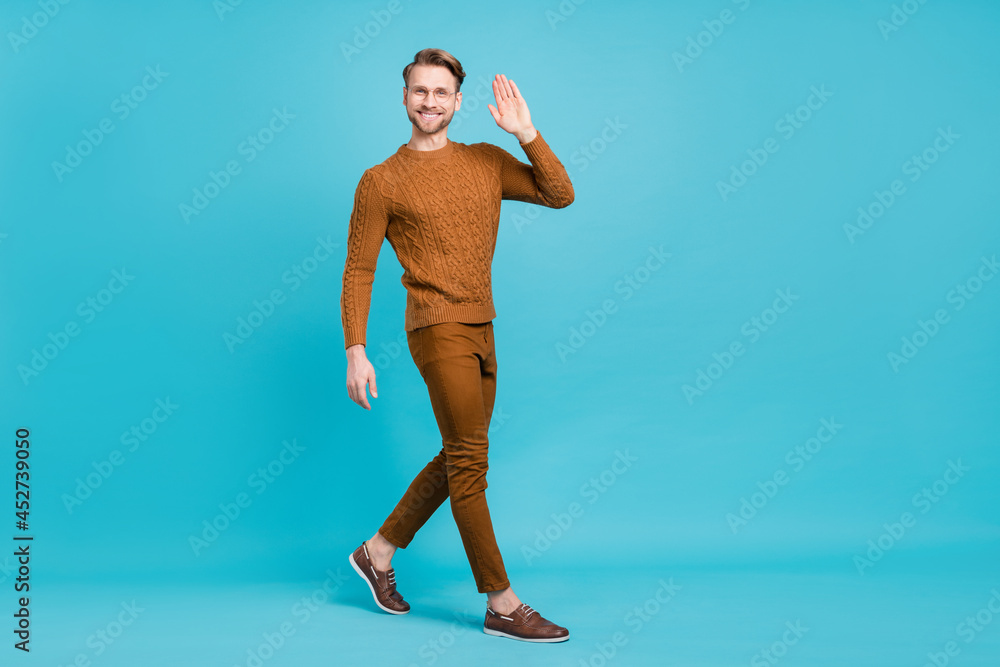 Full body photo charming happy young man walk go empty space wave hello isolated on blue color background Full body photo charming happy young man walk go empty space wave hello isolated on blue color background