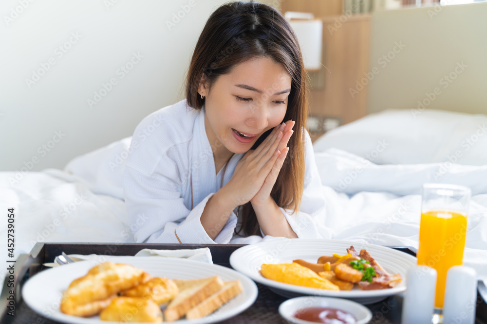Portrait beautiful young Asian woman wearing bathrobe enjoy breakfast on a bed in bedroom