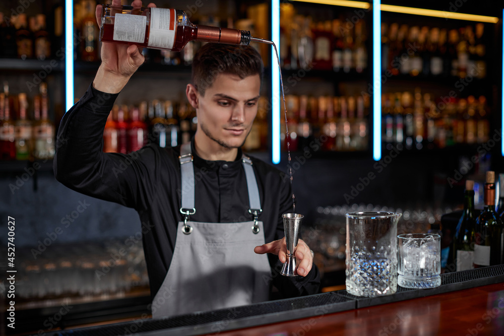 Bartender in apron adds ingredient to glass