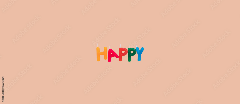 Word Happy spelled with colourful cake candles isolated on a pastel pink background banner with copy space for text. Happy birthday card concept.