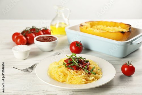 Tasty spaghetti squash with tomato sauce and arugula served on white wooden table