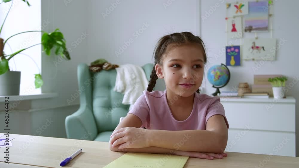 Home distance schooling for kids. Spbd Happy little girl with mole on cheek nods head and talks at videochat at table in children room camera view Home distance schooling for kids. Spbd Happy little girl with mole on cheek nods head and talks at videochat at table in children room camera view