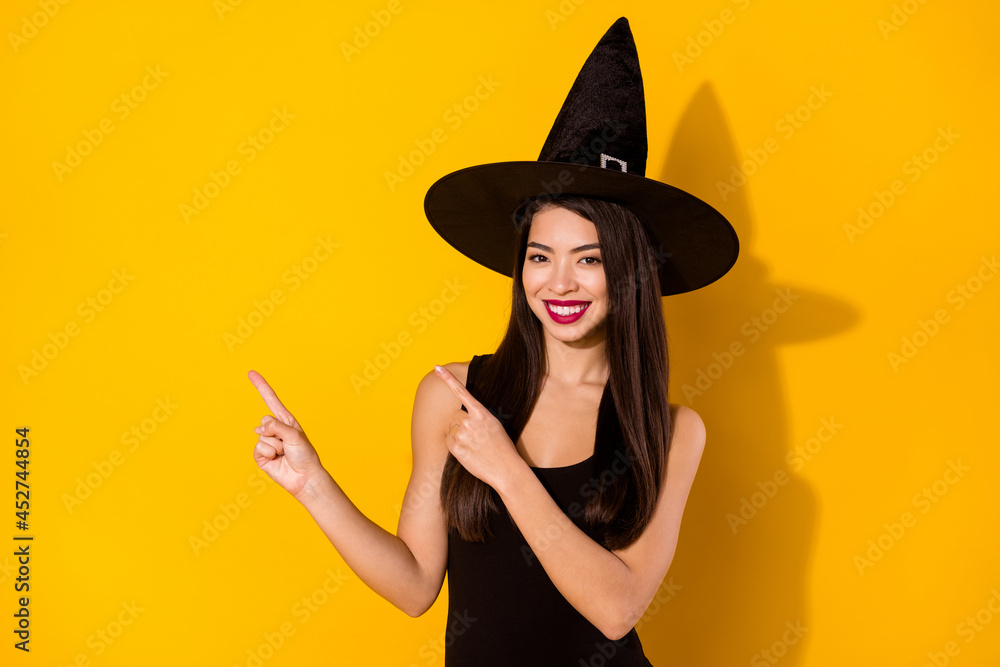 Photo of optimistic millennial brunette hairdo lady point empty space wear black dress witch cap isolated on yellow color background Photo of optimistic millennial brunette hairdo lady point empty space wear black dress witch cap isolated on yellow color background