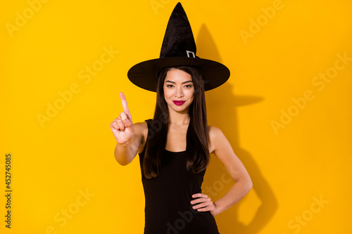 Photo of lovely young brunette hairdo lady finger up wear black dress witch cap isolated on yellow color background photo