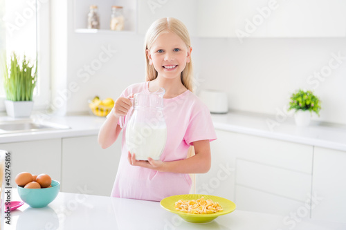 Photo of young attractive little girl happy positive smile breakfast morning meal cornflakes milk cereal home