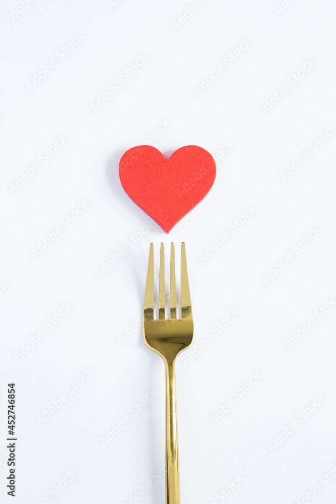 Red heart and gold fork on the white background. Copy space.Top view. Red heart and gold fork on the white background. Copy space.Top view.