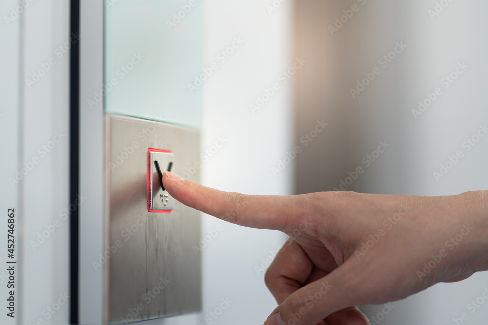 Naklejka premium Action of human is pressing on button switch for call the elevator. Close-up and selective focus at the human's finger.