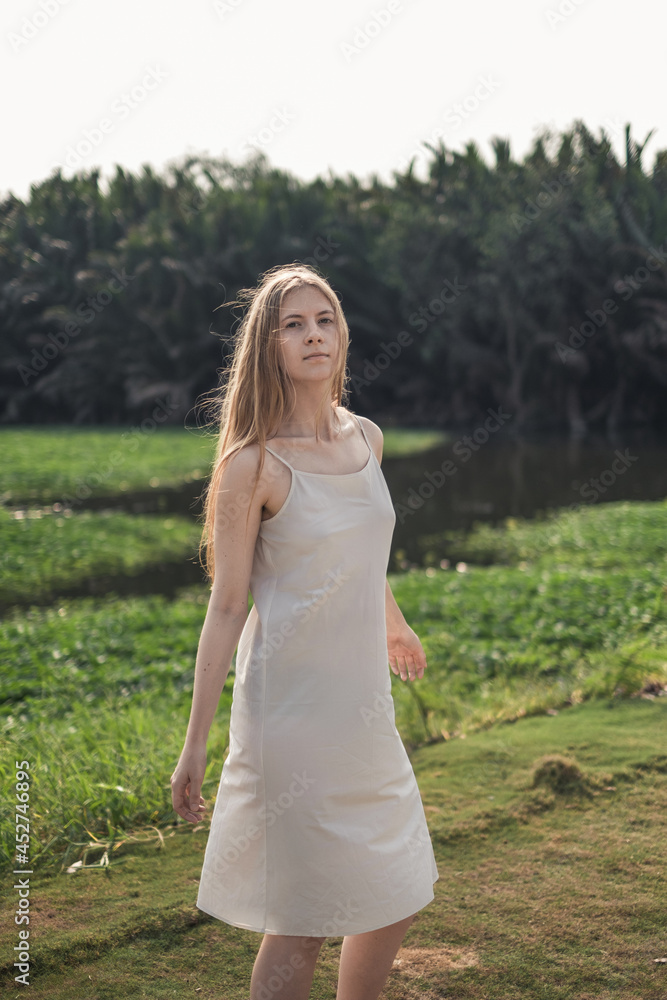 Portrait of pretty caucasian woman in white dress walking in the park and smiling. Long blond hair. Natural beauty. make-up free. beautiful sunshine Portrait of pretty caucasian woman in white dress walking in the park and smiling. Long blond hair. Natural beauty. make-up free. beautiful sunshine