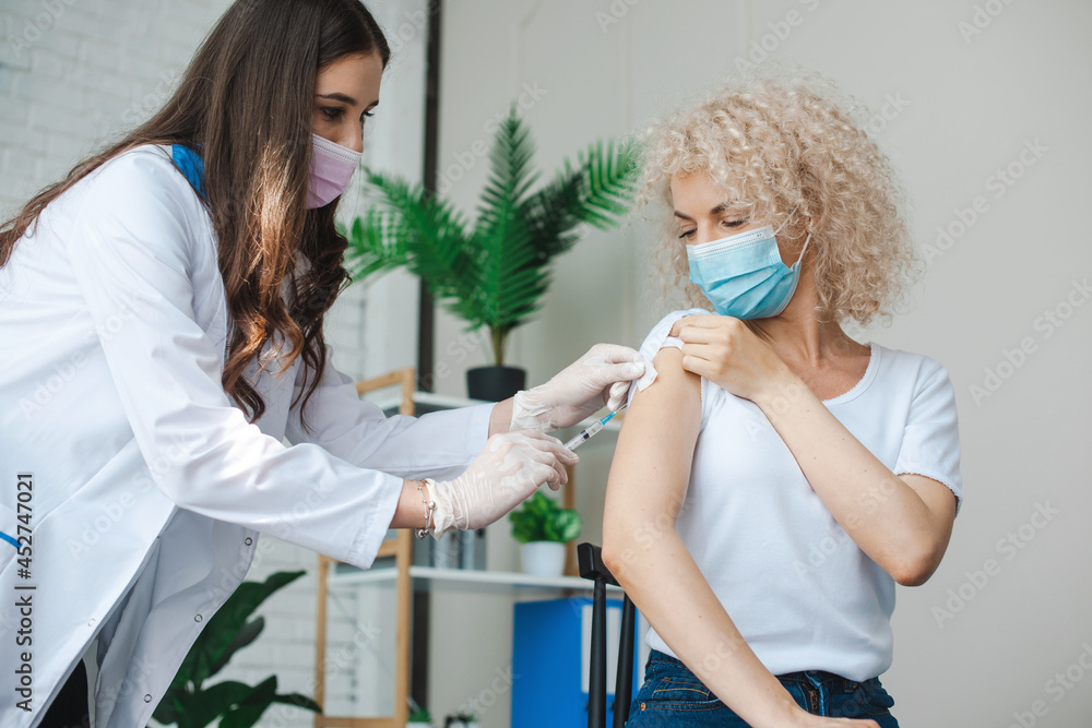 Woman with medical mask putting vaccine for health concept. Doctor giving corona virus vaccine injection to patient. Antiviral vaccine. Covid19 immunization Woman with medical mask putting vaccine for health concept. Doctor giving corona virus vaccine injection to patient. Antiviral vaccine. Covid19 immunization