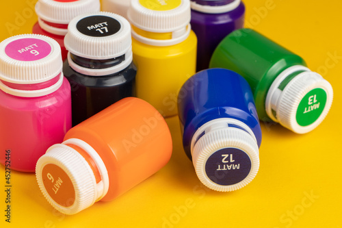 Bottles with multicolored paints on yellow background