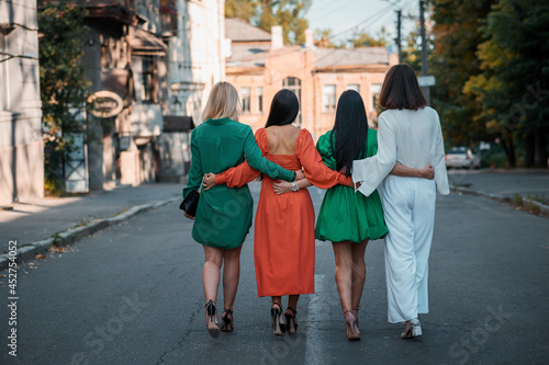 Street Fashion. Four beautiful fashionable girlfriends walk in sunny weather in the city. 