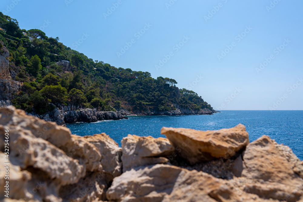 Stony coast from rocks and green trees and bushes by the sea, concept of vacation 