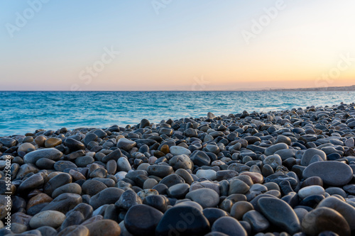 Stony pebble beach in sunset mood and blue sea water, concept of vacation, wanderlust and freedom 