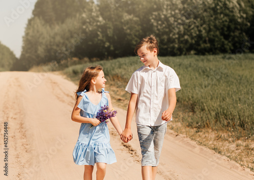 Little girl and boy brother and sister holding hands in nature on a sunny day. Kids in the country.