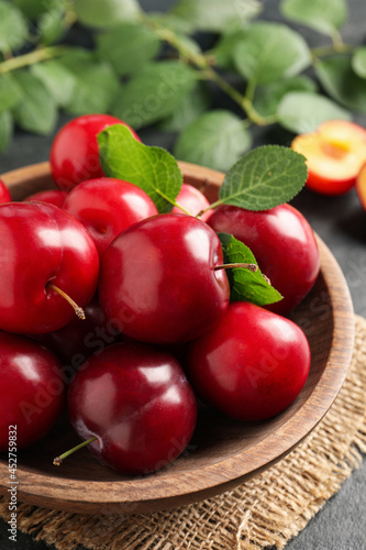 Delicious ripe cherry plums with leaves on black table, closeup