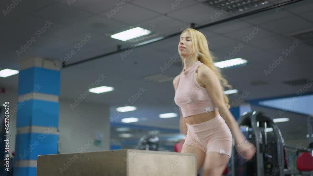 Blond slim beautiful sportswoman with flower tattoo on leg making steps on gym cube indoors. Motivated confident fit Caucasian millennial woman training indoors. Sport and fitness concept Blond slim beautiful sportswoman with flower tattoo on leg making steps on gym cube indoors. Motivated confident fit Caucasian millennial woman training indoors. Sport and fitness concept