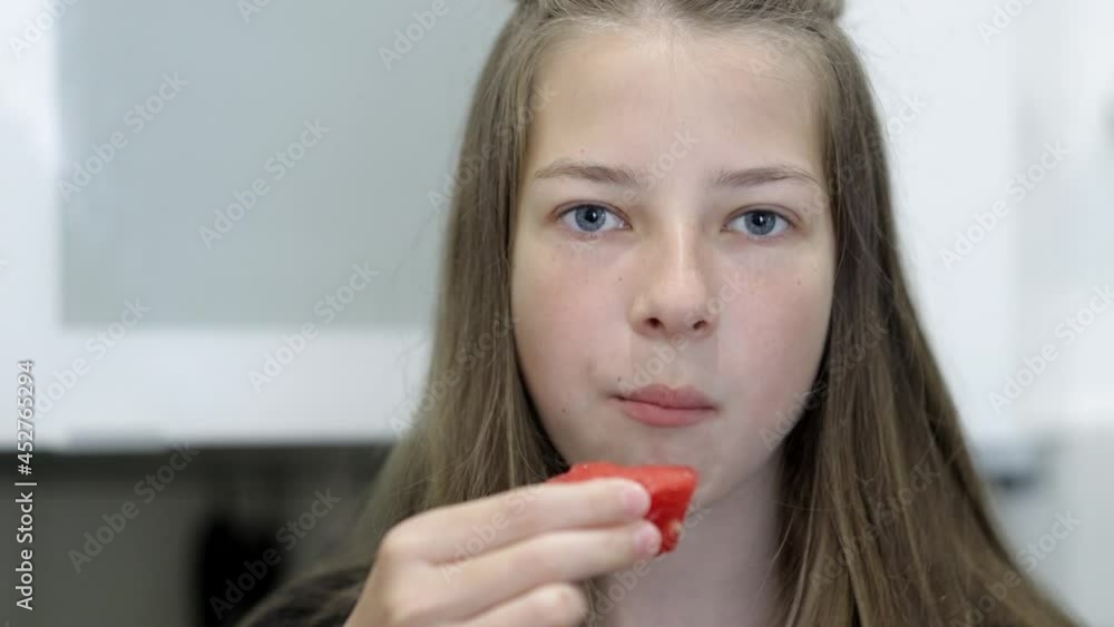 a teenage girl eats a watermelon in the kitchen, sitting at the table a teenage girl eats a watermelon in the kitchen, sitting at the table