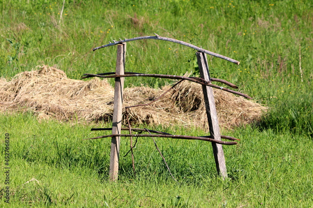 Old wooden support frame made of dry wooden boards and sticks used as support for freshly planted trees on side of small hill in local family house backyard surrounded with dry hey and uncut grass on Old wooden support frame made of dry wooden boards and sticks used as support for freshly planted trees on side of small hill in local family house backyard surrounded with dry hey and uncut grass on