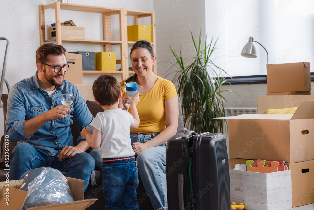 Happy young family husband, wife, and toddler son just moved into new home unpacking. Relocation. Celebrating with a glass of wine. Happy young family husband, wife, and toddler son just moved into new home unpacking. Relocation. Celebrating with a glass of wine.