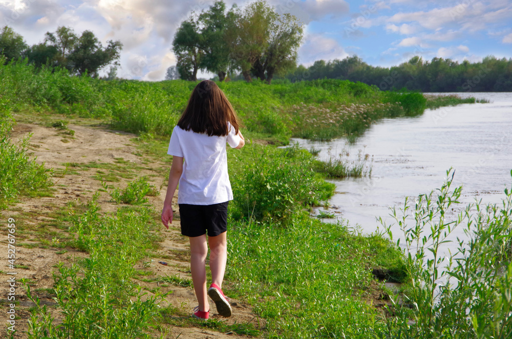 The girl is running along the river on the green grass among dense vegetation. The girl is running along the river on the green grass among dense vegetation.